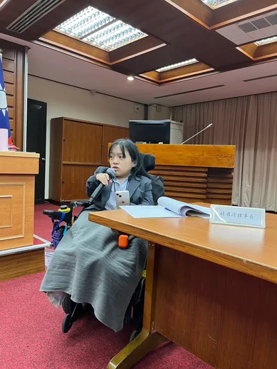 林君潔坐在電動輪椅上，手拿著麥克風正在發言。